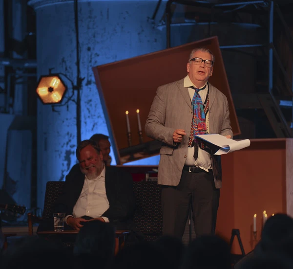 Forfatter Frode Gryttens alter ego Arne Hesjedal står på scenen i Lindehuset, Odda, og leser fra et manus. Foto.